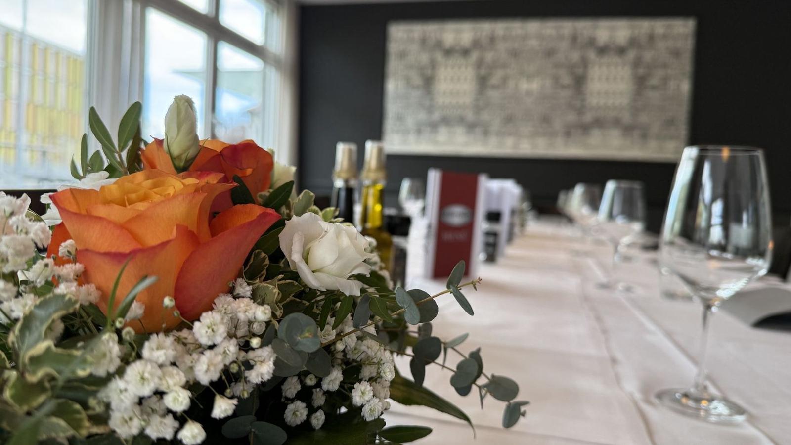Blumengesteck mit orangefarbenen Rosen auf der gedeckten Tafel