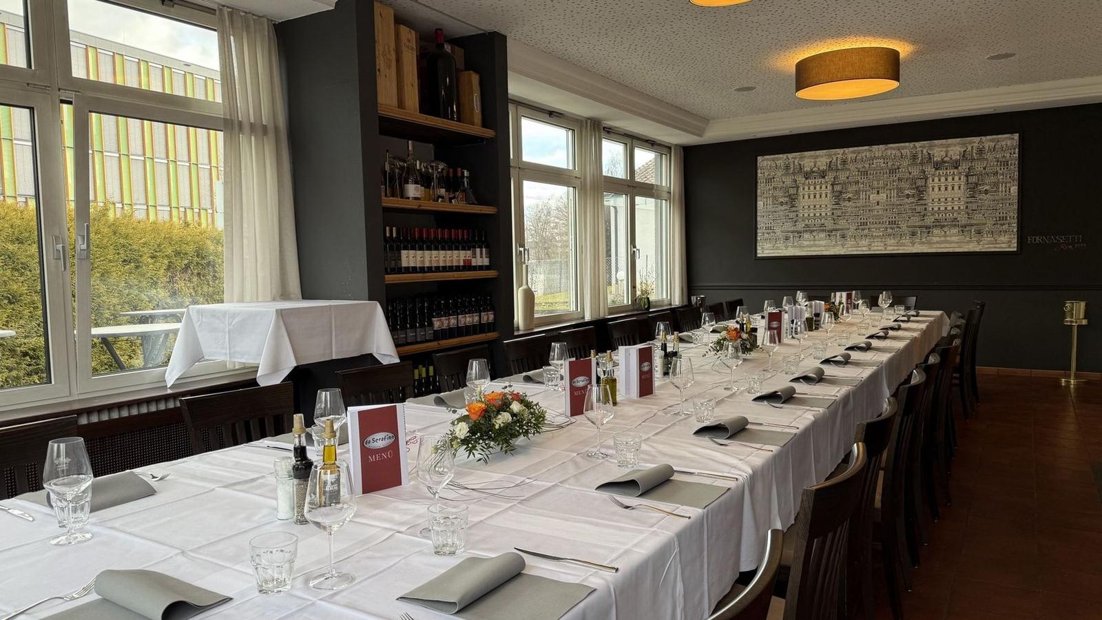 Lange festlich gedeckte Tafel mit Blumengestecken und da-Serafino-Menükarten im Gastraum