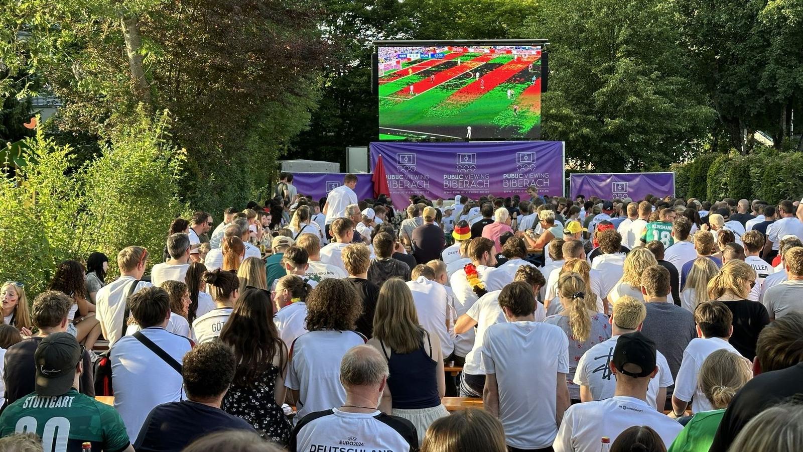 Fans in Trikots in der Abendsonne vor der Leinwand von Public Viewing Biberach